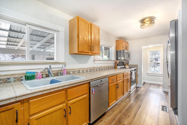 kitchen with appliances with stainless steel finishes, sink, tile countertops, and light wood-type flooring