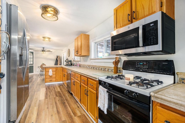 kitchen with sink, light hardwood / wood-style flooring, appliances with stainless steel finishes, kitchen peninsula, and ceiling fan