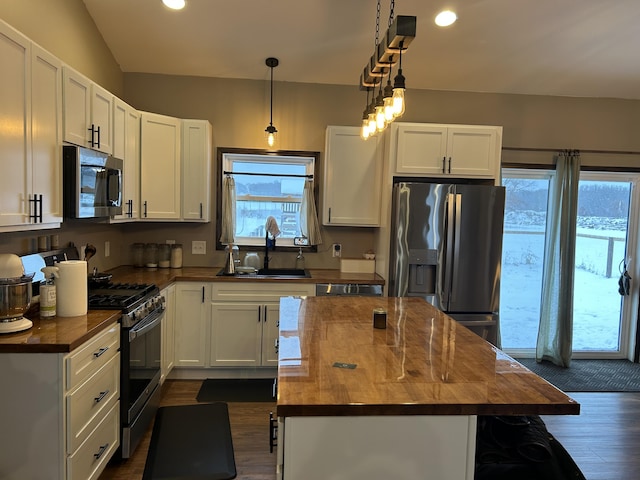 kitchen featuring white cabinetry, a center island, butcher block countertops, pendant lighting, and appliances with stainless steel finishes