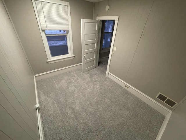 carpeted spare room featuring wood walls