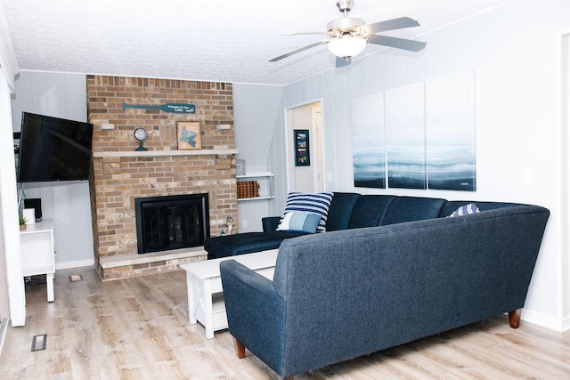 living room featuring a textured ceiling, ceiling fan, ornamental molding, light wood-type flooring, and a brick fireplace