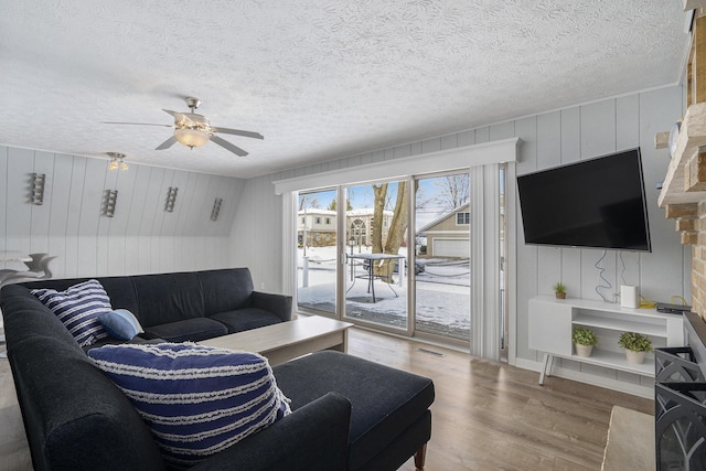 living room with ceiling fan, wooden walls, a textured ceiling, and hardwood / wood-style flooring