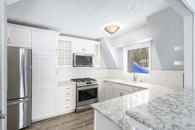 kitchen with white cabinetry, appliances with stainless steel finishes, decorative backsplash, light stone countertops, and sink