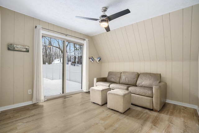 living room featuring a textured ceiling, vaulted ceiling, wood walls, light wood-type flooring, and ceiling fan