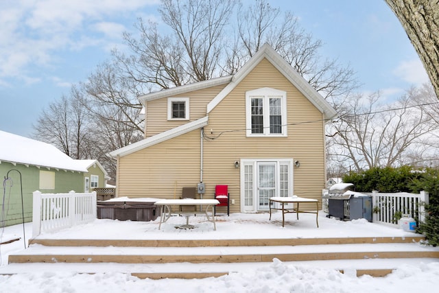 snow covered back of property featuring a wooden deck and a hot tub