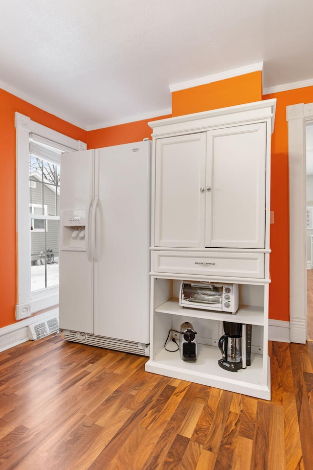 interior space featuring white refrigerator with ice dispenser, hardwood / wood-style floors, white cabinets, and ornamental molding