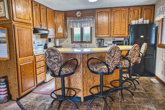 kitchen featuring sink, white electric range, a kitchen breakfast bar, black fridge, and decorative backsplash