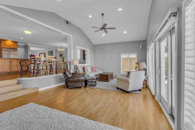 living room featuring ceiling fan with notable chandelier, light hardwood / wood-style flooring, and vaulted ceiling