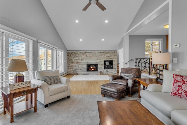 living room featuring vaulted ceiling, ceiling fan, plenty of natural light, and a stone fireplace