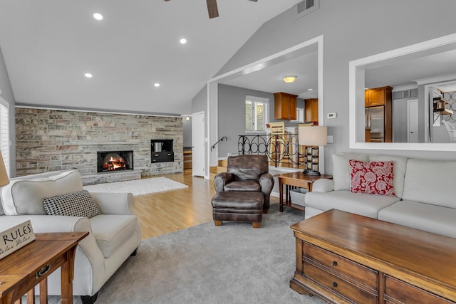 living room featuring ceiling fan, light hardwood / wood-style flooring, a stone fireplace, and lofted ceiling