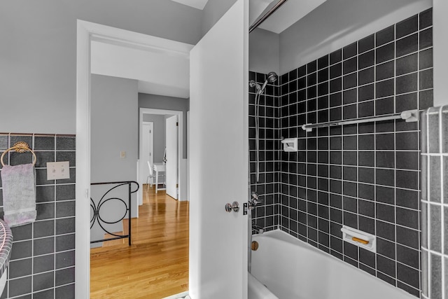 bathroom with tiled shower / bath combo, wood-type flooring, and tile walls