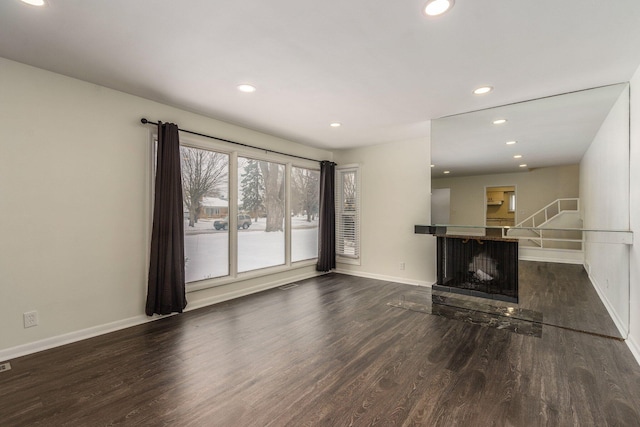 unfurnished living room featuring a multi sided fireplace, recessed lighting, baseboards, and wood finished floors