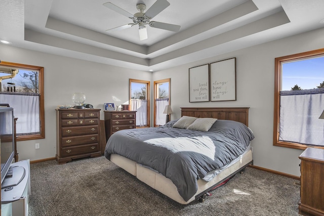 bedroom featuring ceiling fan, a tray ceiling, and dark colored carpet