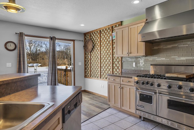 kitchen with light tile patterned floors, appliances with stainless steel finishes, backsplash, light brown cabinetry, and wall chimney exhaust hood