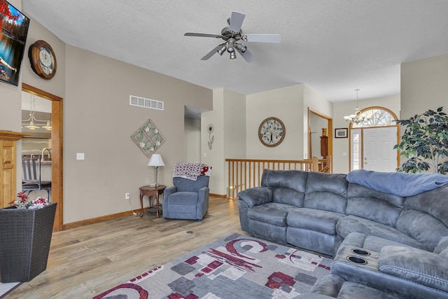 living room featuring ceiling fan with notable chandelier, a textured ceiling, and light hardwood / wood-style flooring