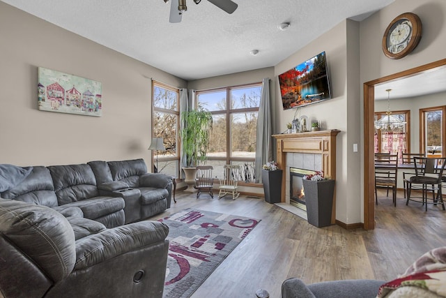 living room with wood-type flooring, ceiling fan with notable chandelier, a tiled fireplace, and a textured ceiling