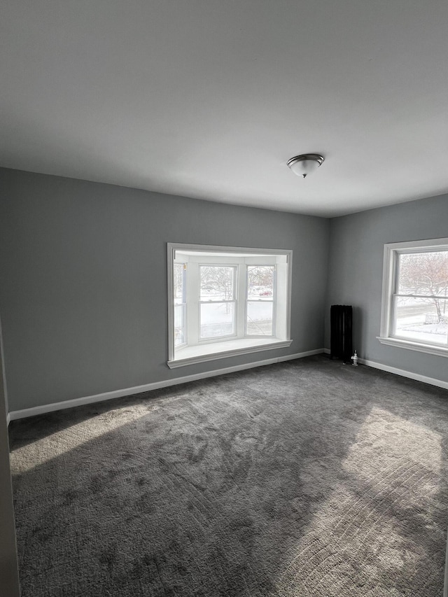 interior space with a wealth of natural light, dark carpet, and radiator heating unit