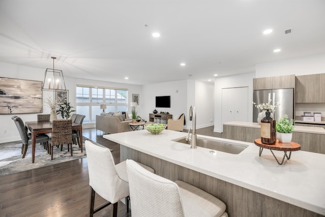 kitchen featuring pendant lighting, dark wood-type flooring, sink, a breakfast bar area, and stainless steel refrigerator