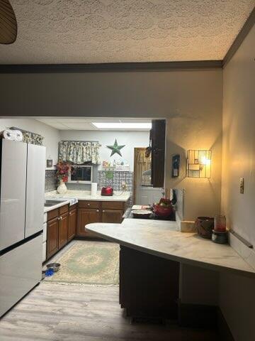 kitchen with hardwood / wood-style floors, crown molding, kitchen peninsula, and stainless steel refrigerator