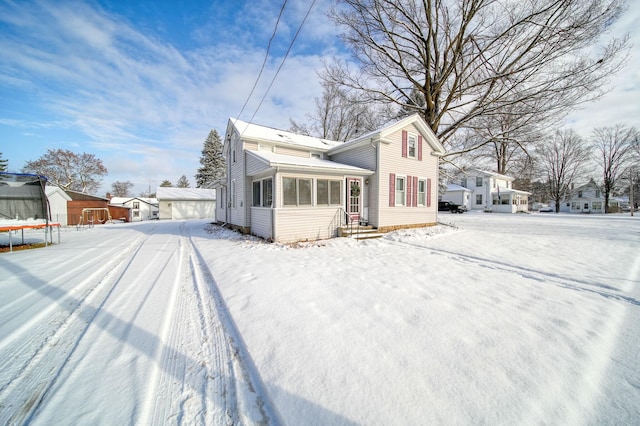 view of snow covered exterior featuring an outbuilding, a trampoline, and a sunroom