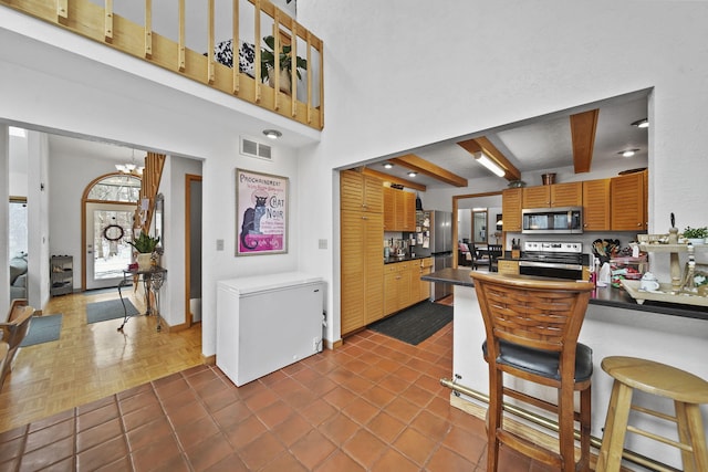 kitchen featuring a towering ceiling, dark parquet floors, stainless steel appliances, a notable chandelier, and beamed ceiling