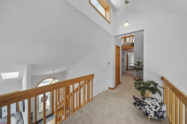 hallway with carpet, a skylight, high vaulted ceiling, and an inviting chandelier