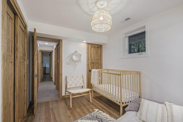 bedroom with a crib, hardwood / wood-style floors, a chandelier, and a closet