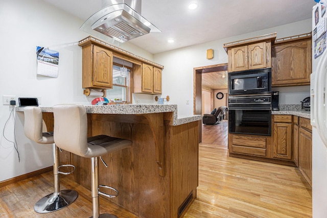 kitchen featuring a kitchen bar, light wood-type flooring, island range hood, and black appliances