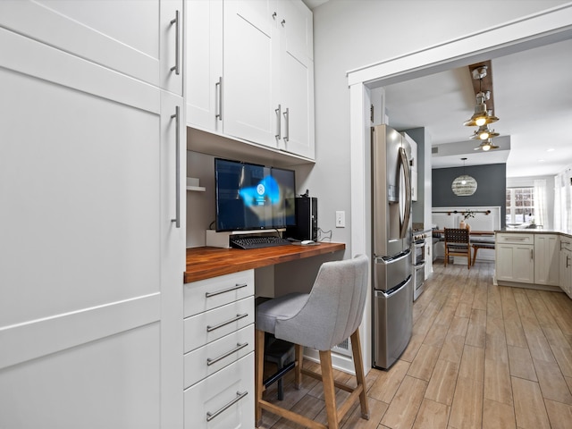 kitchen featuring decorative light fixtures, butcher block counters, light hardwood / wood-style floors, stainless steel refrigerator with ice dispenser, and white cabinets