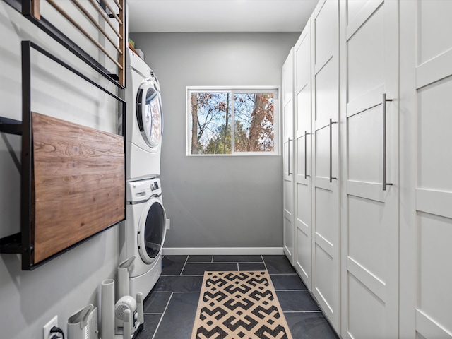 laundry area featuring stacked washer / drying machine and dark tile patterned flooring