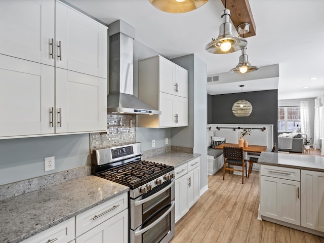 kitchen featuring white cabinets, wall chimney exhaust hood, light hardwood / wood-style floors, double oven range, and pendant lighting