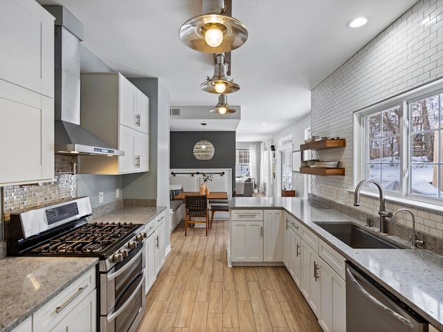 kitchen with sink, wall chimney range hood, white cabinetry, and appliances with stainless steel finishes