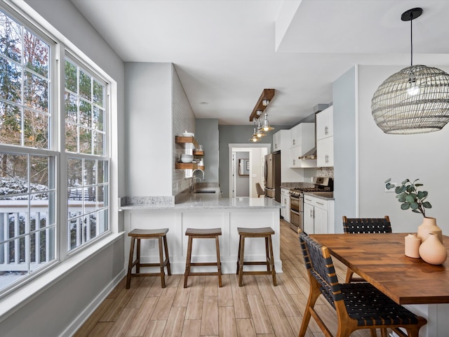 kitchen featuring a kitchen breakfast bar, appliances with stainless steel finishes, kitchen peninsula, white cabinets, and sink