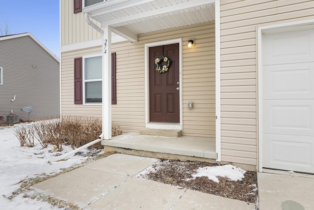 snow covered property entrance featuring a garage and central air condition unit