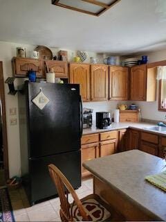 kitchen featuring black refrigerator, light tile patterned floors, and sink