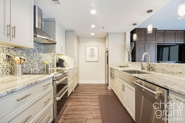 kitchen featuring appliances with stainless steel finishes, wall chimney range hood, pendant lighting, white cabinets, and dark hardwood / wood-style floors