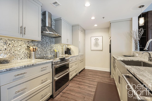 kitchen with dark hardwood / wood-style flooring, stainless steel appliances, light stone counters, and wall chimney exhaust hood