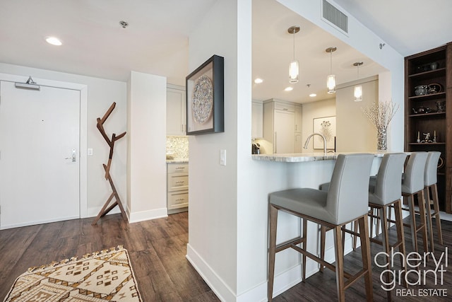 kitchen with hanging light fixtures, tasteful backsplash, dark hardwood / wood-style floors, kitchen peninsula, and a kitchen bar