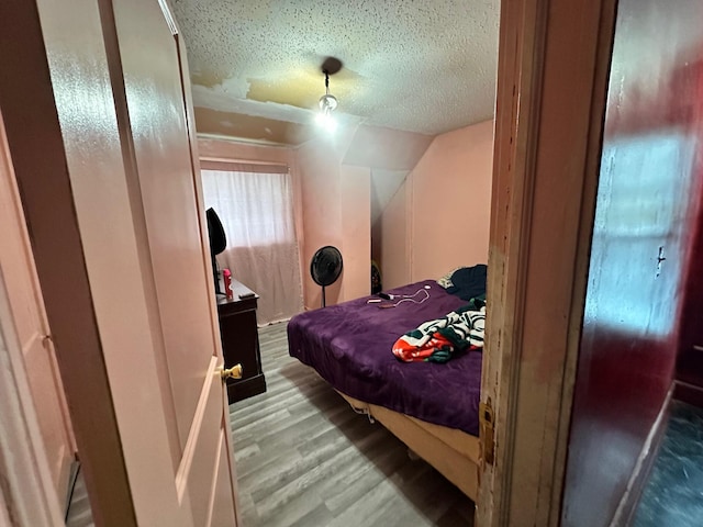 bedroom with a textured ceiling, light wood-type flooring, and vaulted ceiling