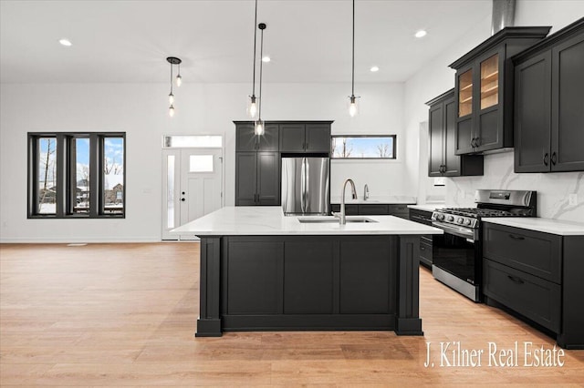 kitchen with decorative backsplash, hanging light fixtures, a kitchen island with sink, light stone counters, and stainless steel appliances