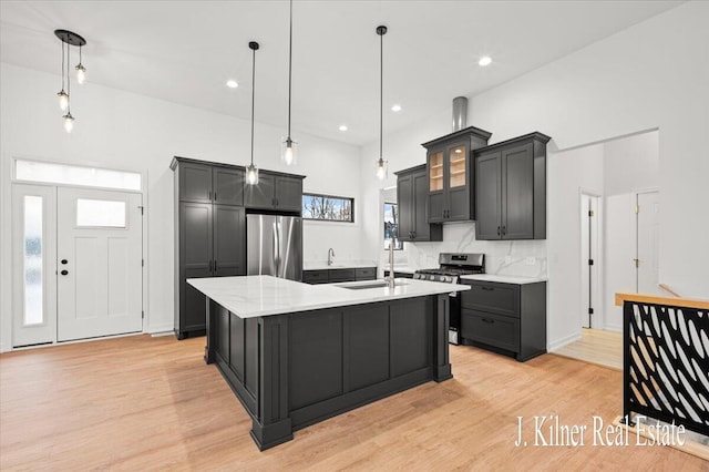 kitchen with stainless steel appliances, a center island with sink, light hardwood / wood-style floors, and decorative light fixtures