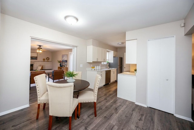 dining area featuring a fireplace, ceiling fan, sink, and dark wood-type flooring