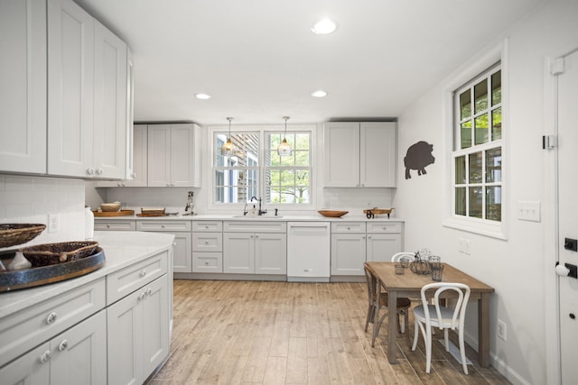 kitchen featuring white dishwasher, tasteful backsplash, hanging light fixtures, and sink