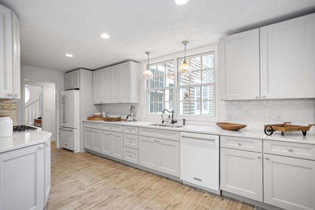 kitchen featuring tasteful backsplash, white appliances, sink, white cabinets, and hanging light fixtures