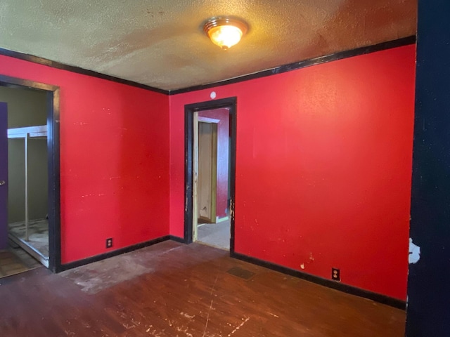 unfurnished room with a textured ceiling, ornamental molding, and dark wood-type flooring