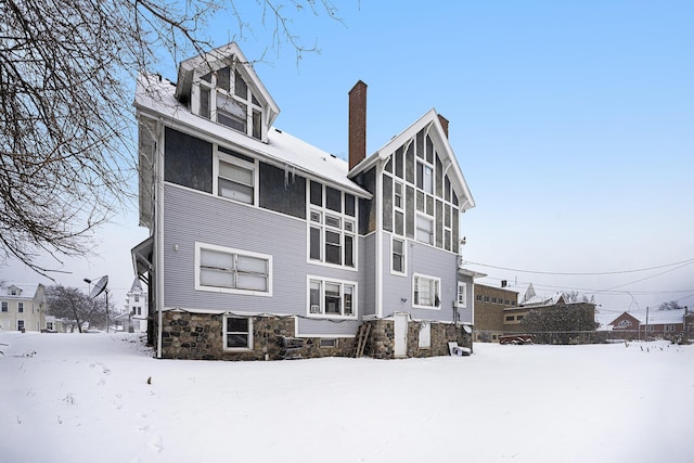 snow covered rear of property featuring a sunroom