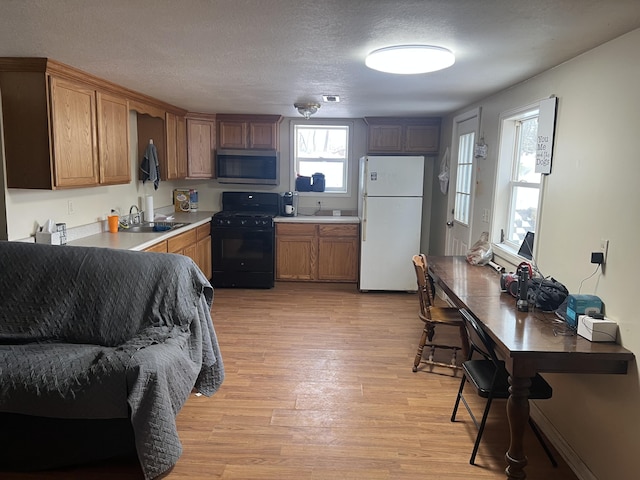 kitchen with white refrigerator, black gas stove, sink, a textured ceiling, and light hardwood / wood-style floors