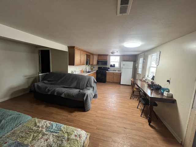 bedroom with white fridge, a textured ceiling, and light wood-type flooring