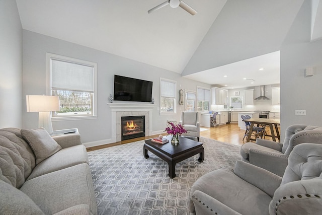 living room featuring light hardwood / wood-style floors, high vaulted ceiling, ceiling fan, and a tiled fireplace