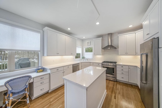 kitchen featuring white cabinetry, a center island, wall chimney range hood, and appliances with stainless steel finishes